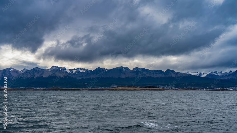 A picturesque mountain range against the background of the sky and dark rain clouds. Ripples on the surface of the water. Argentina. Beagle Channel