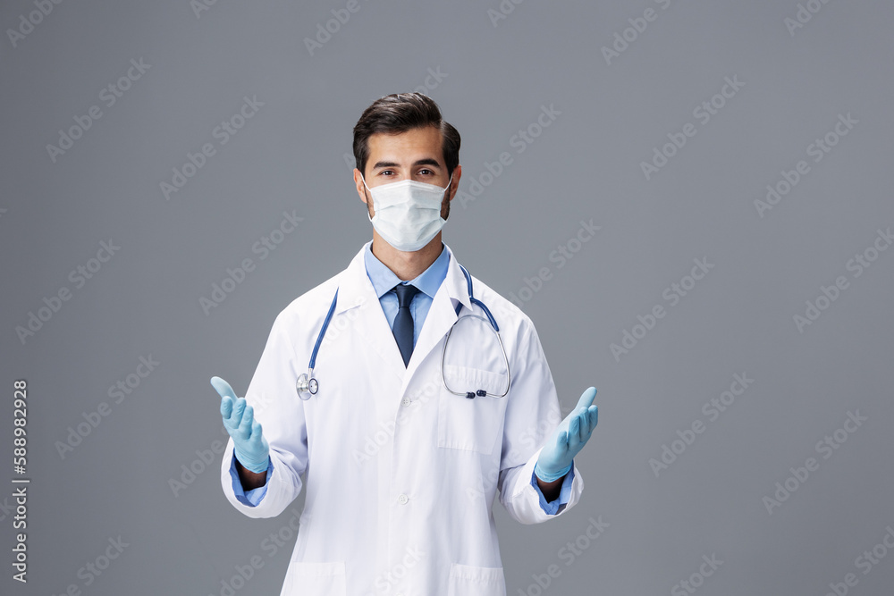 Male doctor in a white coat and medical mask and sterile gloves, eyeglasses looks at the camera on a gray isolated background, copy space, space for text, health Male doctor in a white coat and medical mask and sterile gloves, eyeglasses looks at the camera on a gray isolated background, copy space, space for text, health