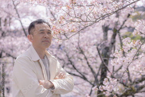 Middle-aged Asian man wearing white cardigan with cherry blossoms in background.