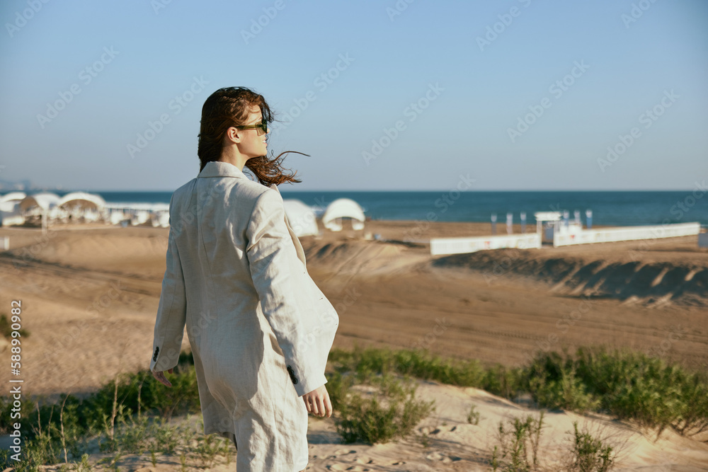 a woman in a light jacket stands with her back to the camera near the sea promenade