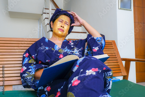 A woman with beauty mask on her face closed her eyes, one hand on her head, an open book on her lap. photo