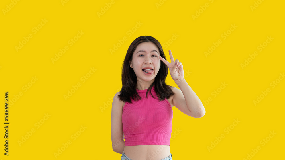 Young Asian woman making two thumbs up gesture showing joy and fun, Symbol of good friendship, Popular photo poses, Make a v-shaped finger, Yellow background. Young Asian woman making two thumbs up gesture showing joy and fun, Symbol of good friendship, Popular photo poses, Make a v-shaped finger, Yellow background.