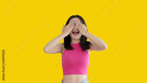 Young woman covering her face and eyes with her hands isolated, Cover your eyes with your hands for fear or prying eyes, Sneak peek, Yellow background.