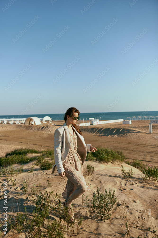 stylish woman walking on the coast in a light jacket and sunglasses in windy weather