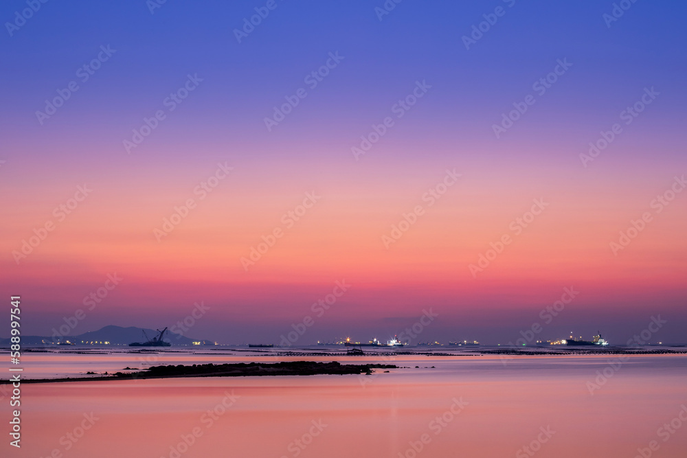 long exposure technic therefore motion blurred effect Smoky and soft sea water surface with small island named Koh Loy boat  rock and commercial vessel container cargo at horizon during sun set