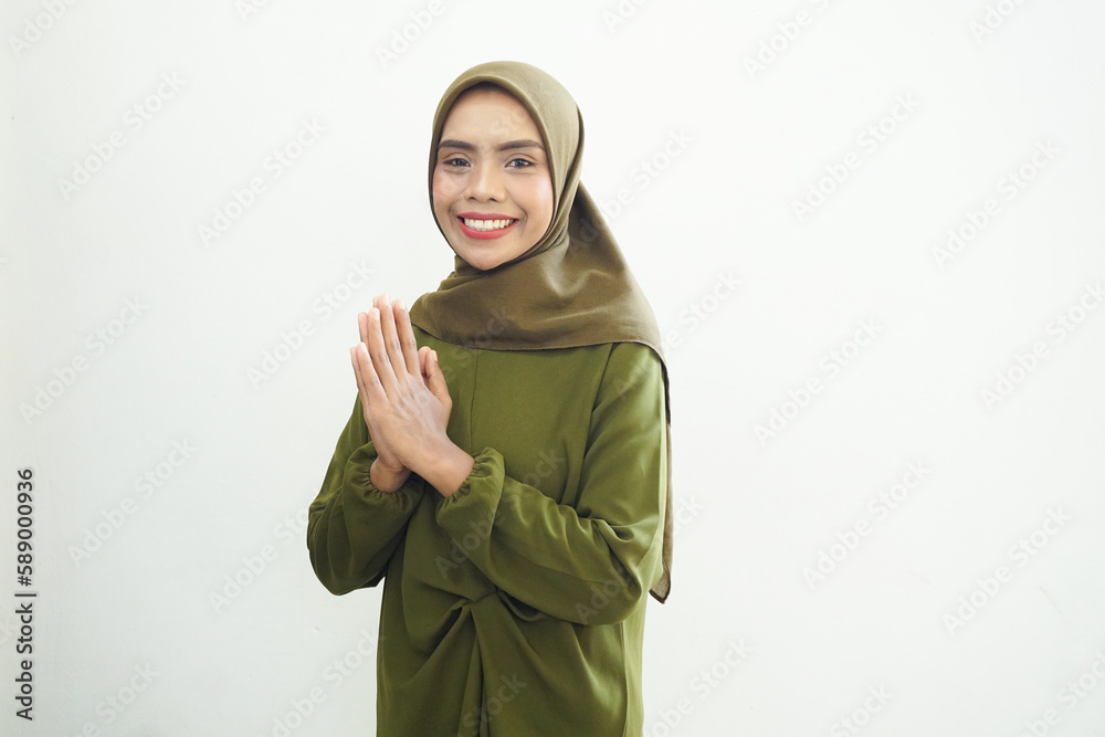 Smiling young Asian Muslim woman in green casual dress and hijab gesturing Eid Mubarak greeting isolated over white background Smiling young Asian Muslim woman in green casual dress and hijab gesturing Eid Mubarak greeting isolated over white background