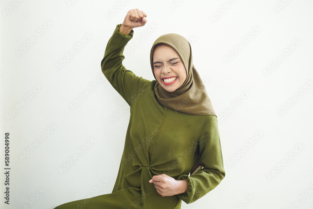 Excited young Asian Muslim woman raising fists and celebrating victory on Ramadan isolated over white background. People religious Islam lifestyle concept Excited young Asian Muslim woman raising fists and celebrating victory on Ramadan isolated over white background. People religious Islam lifestyle concept
