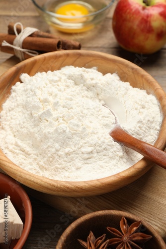 Bowl with flour and ingredients on wooden table, closeup. Yeast pastry