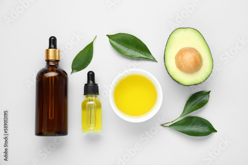 Essential oil, fresh cut avocado and leaves on white background, flat lay