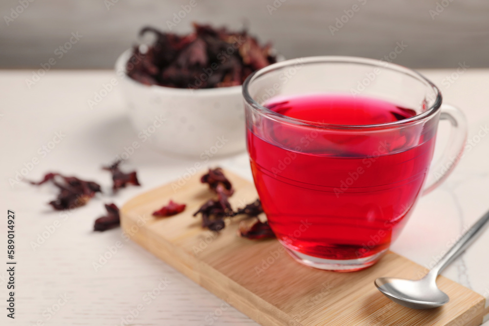 Cup of fresh hibiscus tea, dry flower leaves and spoon on wooden table. Space for text Cup of fresh hibiscus tea, dry flower leaves and spoon on wooden table. Space for text