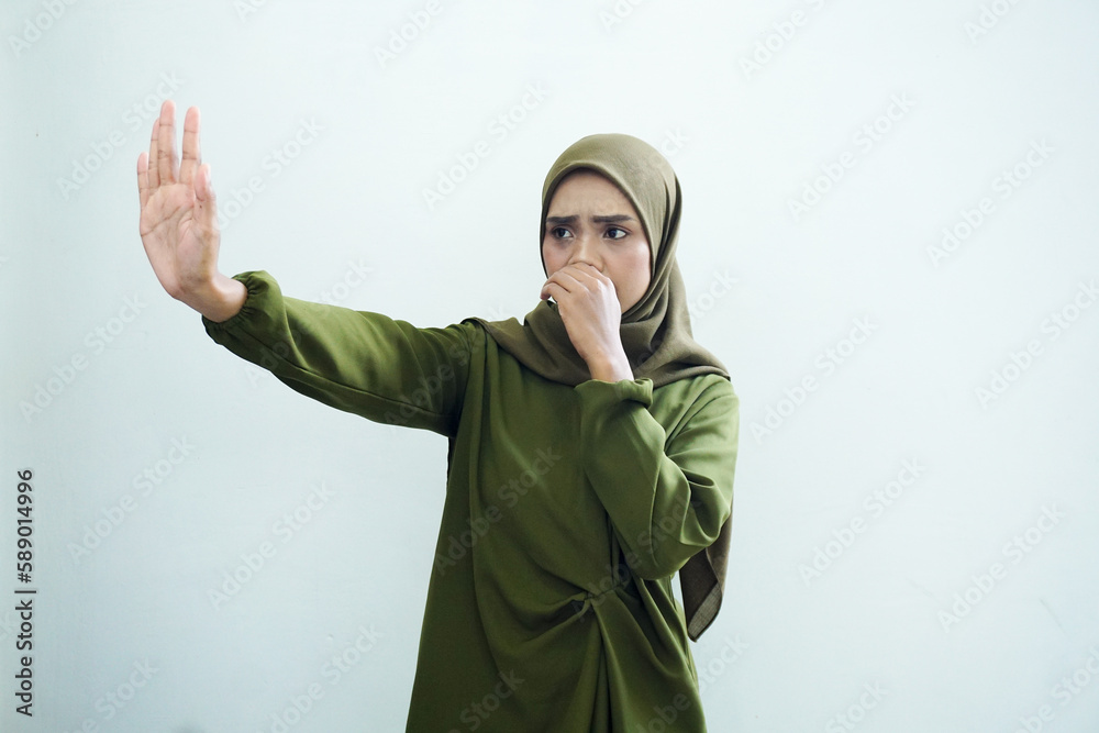 Beautiful young Asian Muslim woman wearing green dress and headscarf covering nose for feeling smell isolated on white background. Religious Islamic lifestyle concept