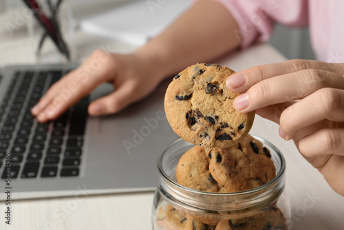 Office worker taking chocolate chip cookie from jar at workplace, closeup