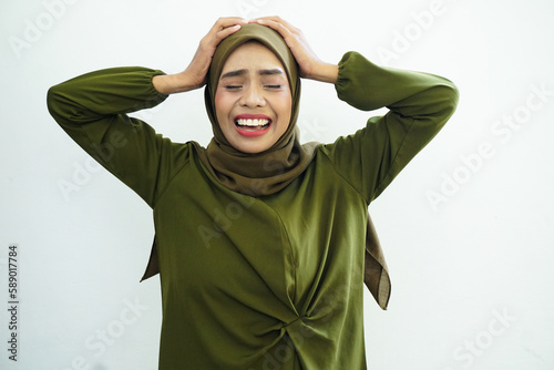 Angry young Asian Muslim man screaming covering ears with both hands, distressed by noise isolated over white background. © rizkiwanggono