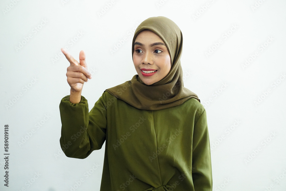 Beautiful young Asian Muslim woman wearing green dress and hijab pointing finger at free space place for an advertisement isolated on white background. People religious Islamic lifestyle concept Beautiful young Asian Muslim woman wearing green dress and hijab pointing finger at free space place for an advertisement isolated on white background. People religious Islamic lifestyle concept