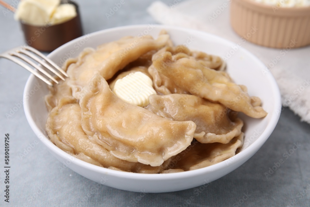 Delicious dumplings (varenyky) with cottage cheese and butter served on light grey table, closeup