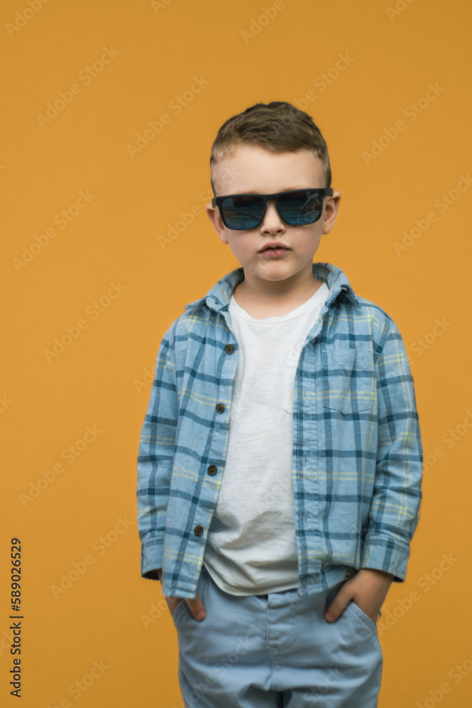 Fashionable little boy in sunglasses. Stylish kid in shirt. Fashion children on orange background. Vertical photo. Fashionable little boy in sunglasses. Stylish kid in shirt. Fashion children on orange background. Vertical photo.