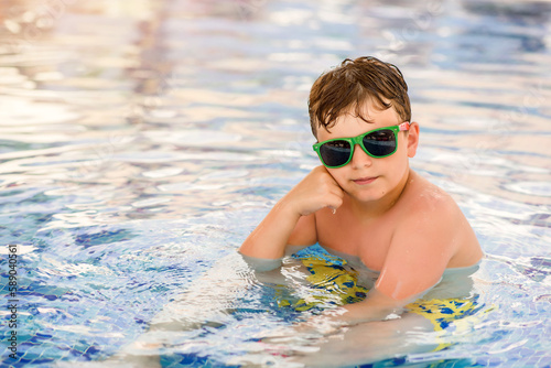 Little boy in sunglasses is swimming and smiling in the swimming pool.