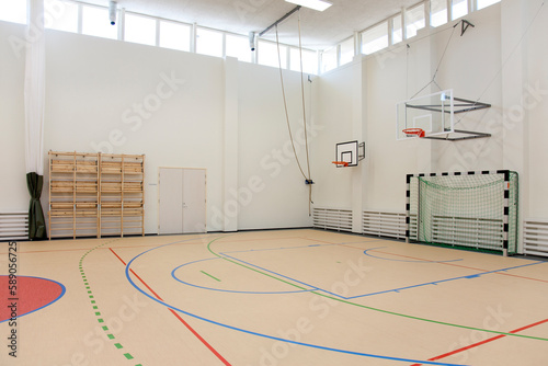 Indoor basketball court at a school. Wooden floor and marked court, a hoop and backboard.