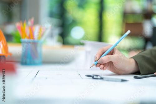 Selective focus, Pencil on hand of female architect designer with blueprint and model construction on desk in office.