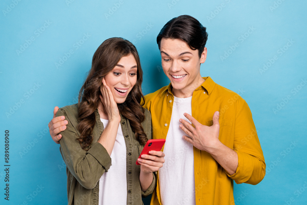 Photo of young excited surprised couple friends amazed hold phone watch funny youtube video content with animals isolated on blue color background Photo of young excited surprised couple friends amazed hold phone watch funny youtube video content with animals isolated on blue color background