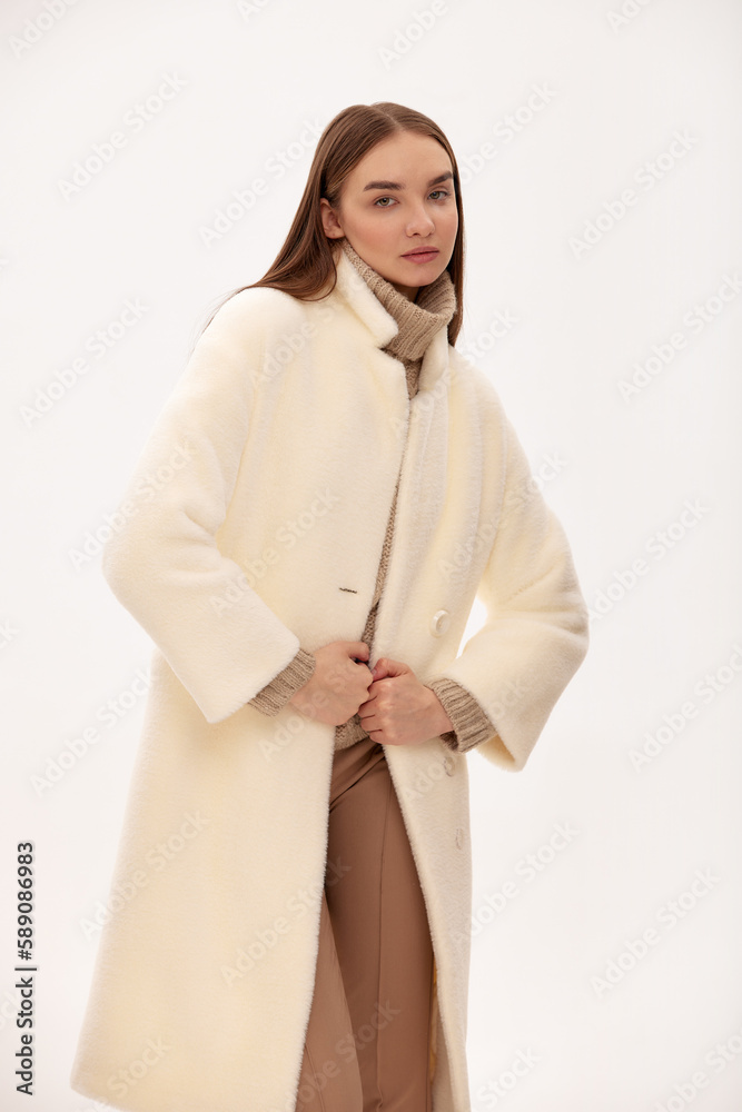 Fashionable self-confident girl in a light faux fur coat. Modern fashion trend for fur coats made of faux fur. Model posing in a fur coat on a light background Fashionable self-confident girl in a light faux fur coat. Modern fashion trend for fur coats made of faux fur. Model posing in a fur coat on a light background