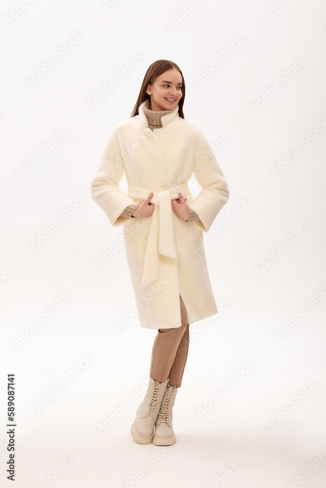 Fashionable self-confident girl in a light faux fur coat. Modern fashion trend for fur coats made of faux fur. Model posing in a fur coat on a light background Fashionable self-confident girl in a light faux fur coat. Modern fashion trend for fur coats made of faux fur. Model posing in a fur coat on a light background