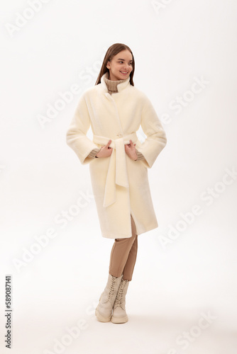 Fashionable self-confident girl in a light faux fur coat. Modern fashion trend for fur coats made of faux fur. Model posing in a fur coat on a light background