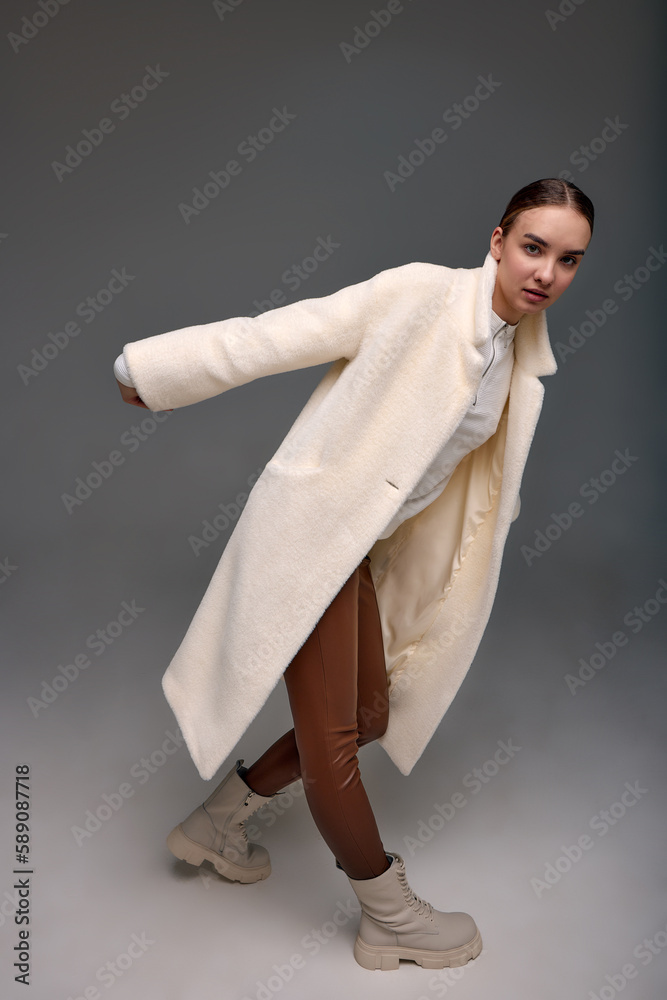 A girl in a light artificial fur coat on a gray background. Modern fashion trend for fur coats made of faux fur. Model posing in a light fur coat on a gray background A girl in a light artificial fur coat on a gray background. Modern fashion trend for fur coats made of faux fur. Model posing in a light fur coat on a gray background