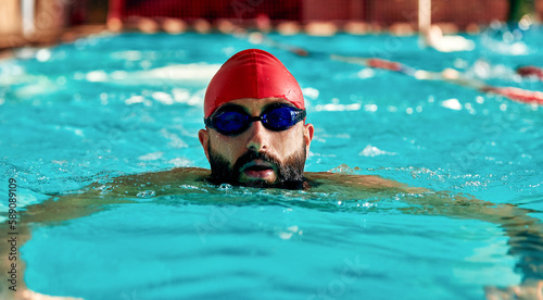 Swimming - male swimmer swimming breaststroke. Close up portrait of man doing breast stroke swimming in pool wearing red swimming cap and swim goggles