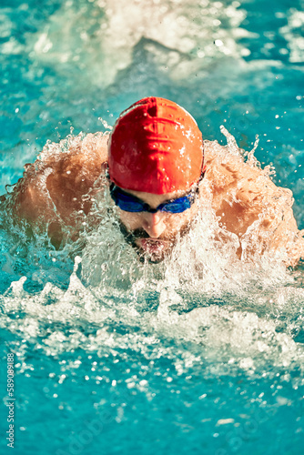Swimming - male swimmer swimming breaststroke. Close up portrait of man doing breast stroke swimming in pool wearing red swimming cap and swim goggles © Georgii