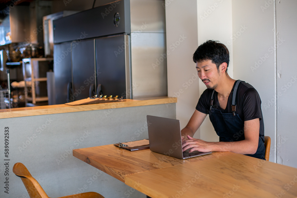 A man seated at a table using a laptop computer, owner and manager of a small restaurant. A man seated at a table using a laptop computer, owner and manager of a small restaurant.