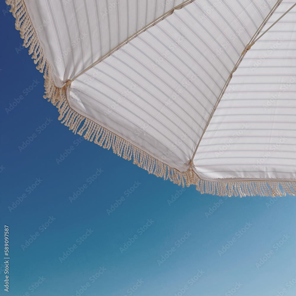 Striped beach umbrella over blue sky - obrazy, fototapety, plakaty 