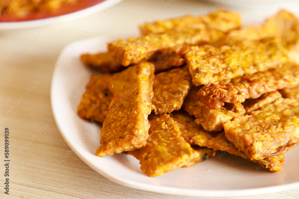 Tempe goreng or fried tempeh is served on a plate along with sambal Tempe goreng or fried tempeh is served on a plate along with sambal