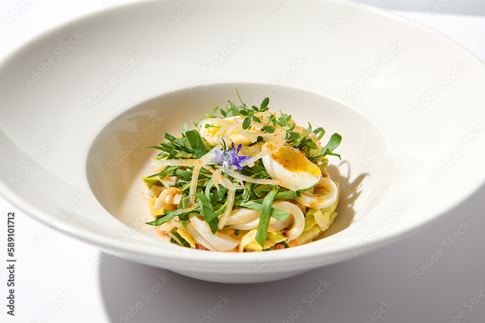 Healthy salad with squid and avocado on white plate with harsh shadows. Calamari salad with vegetables and eggs on white background with shadows of leaves. Summer food menu. Healthy salad with squid and avocado on white plate with harsh shadows. Calamari salad with vegetables and eggs on white background with shadows of leaves. Summer food menu.
