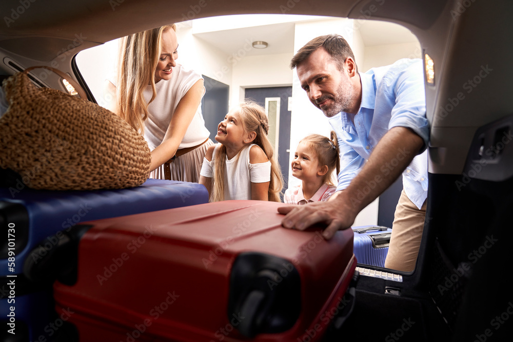 Caucasian family of four packing luggage into car trunk for holiday