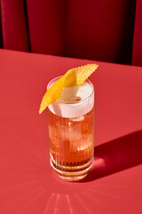 Classic cocktail whiskey sour with egg foam in highball glass on red background. Whiskey sour on coloured background in trendy style. Contemporary concept with alcohol beverage with shadow.
