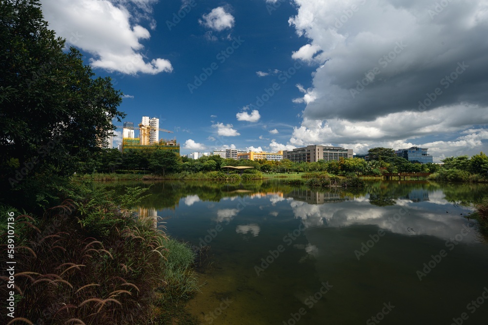Sky clouds with reflection in a lake surrounded by trees and buildings in the background