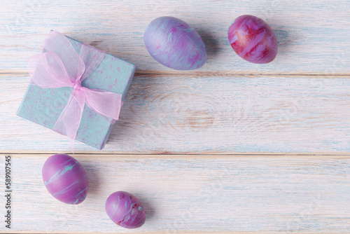 Painted Easter eggs and gift box on wooden background with copy space. Trendy fluid art decoration. Easter holiday concept