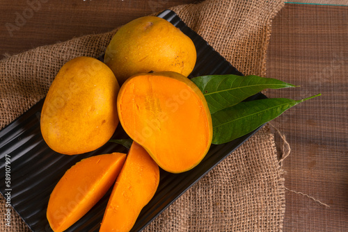 Ripe yellow Mango with cut in half and green leaf isolated on wooden background.
