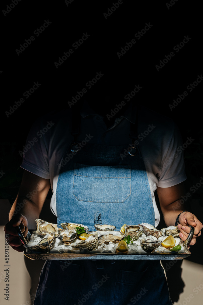 waiter holding a metal tray fresh raw oysters with lime, lemon and ice. raw opened oyster, lifestyle food, ready to eat. Oyster dinner in restaurant