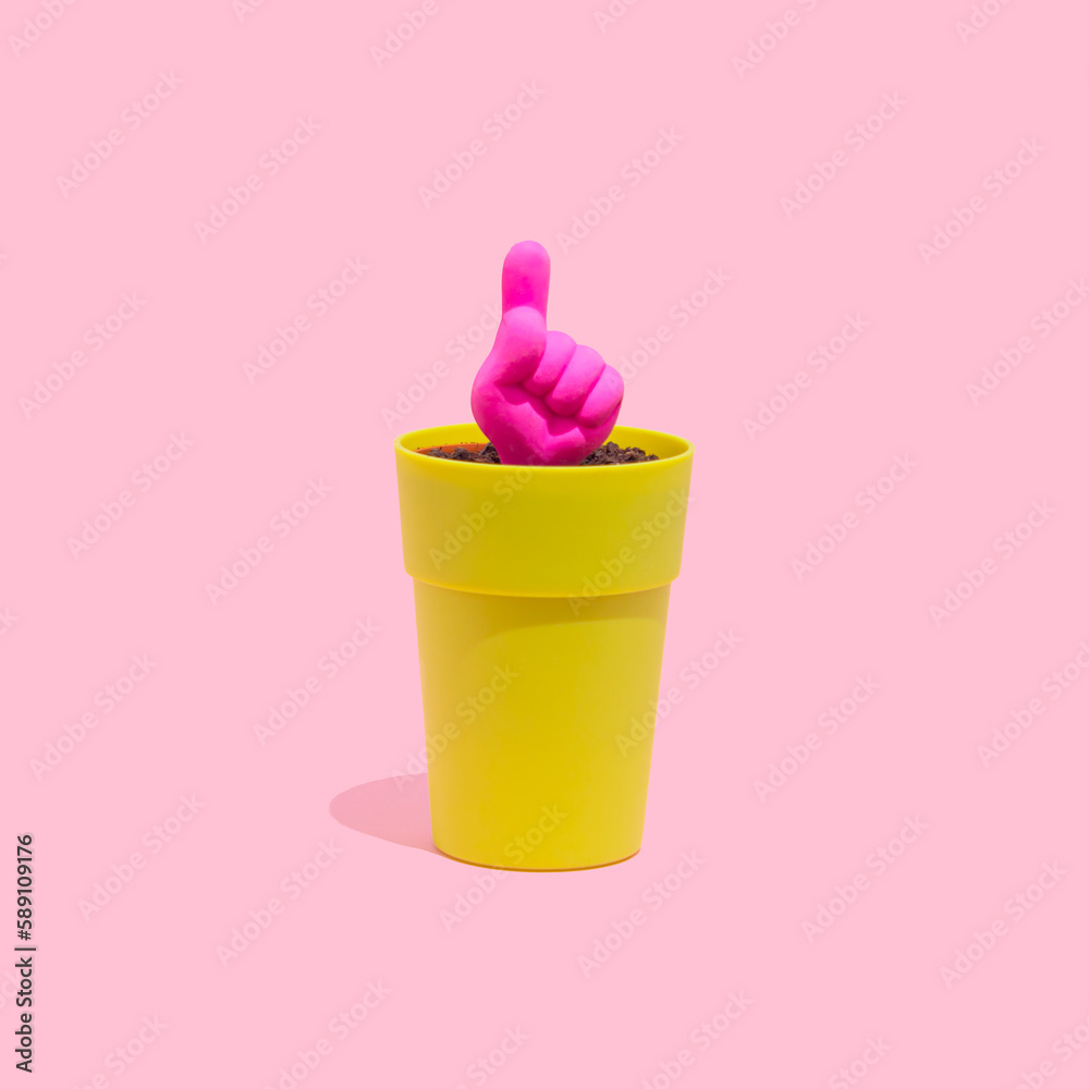 One finger up icon growing from a small pot on a pastel pink background. Hand gesture concept. One finger up icon growing from a small pot on a pastel pink background. Hand gesture concept.