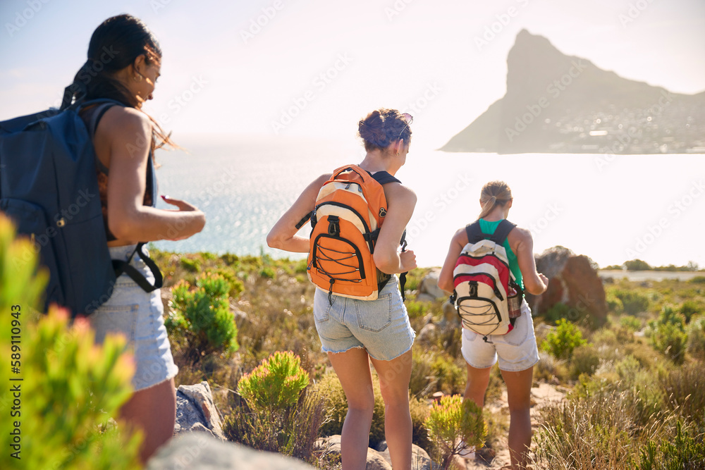 Rear View Of Female Friends With Backpacks On Vacation On Hike Through Countryside Next To Sea