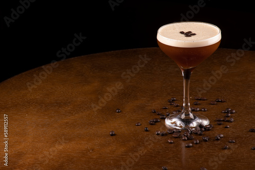 espresso martini cocktail in glass served under rubber holder with spilled coffee beans on table