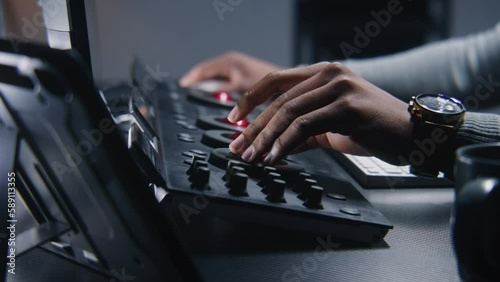Hands close up of African American colorist working by color grading control panel in studio with modern design. Film editor makes colour correction for video post production. Professional equipment.