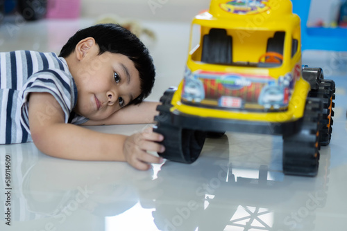 Lovely Asian baby boy playing with yellow toy car on floor at home.