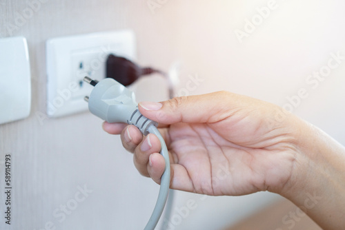 Women's hand plug in or putting  in electricity socket  on wooden floor with sun warm light. photo