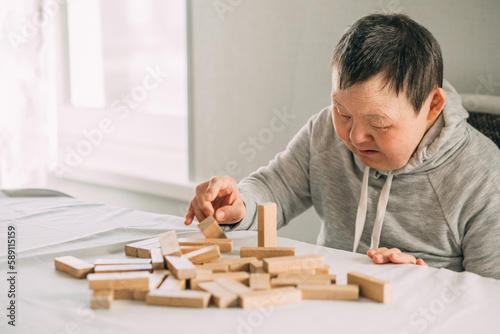 elderly woman with down syndrome and an Asian girl play in tower from wooden blocks
