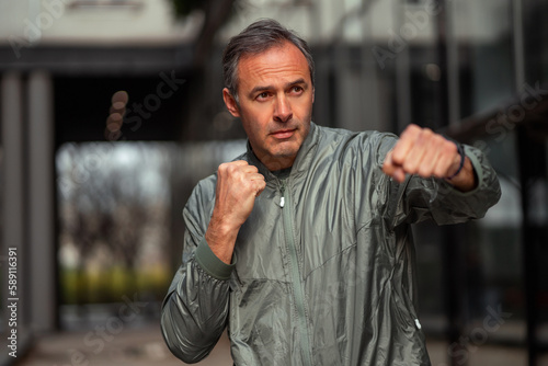 A middle-aged man is working out outdoors in the city, he is doing cardio exercises and boxing moves.