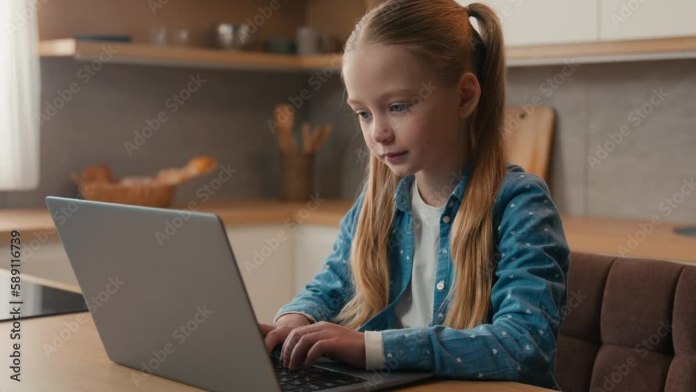 Caucasian little school girl child baby kid schoolgirl daughter at home kitchen using laptop browsing chatting study internet lesson class studying learning distant with computer playing online game
