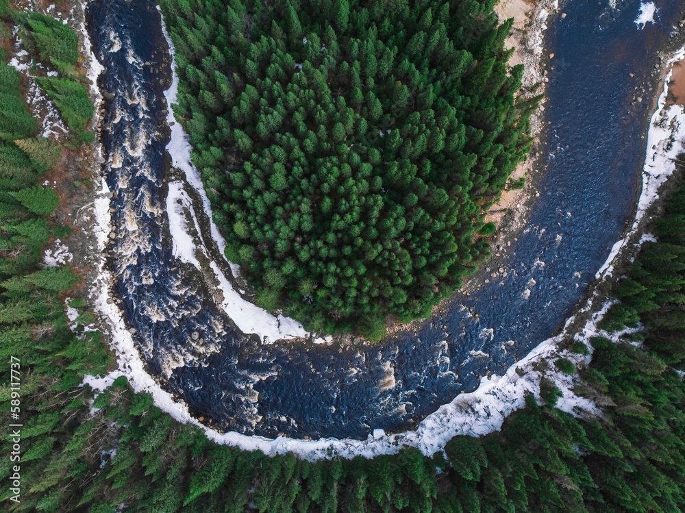 Naklejka premium Aerial view of a river surrounded by trees and snow in Quebec, Canada